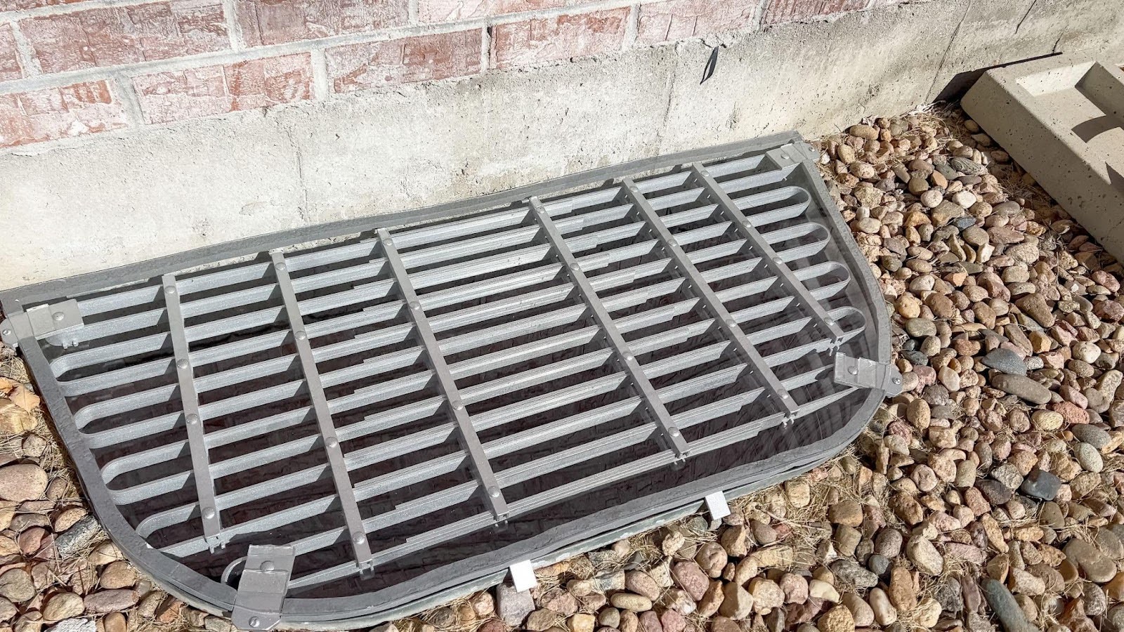 A metal grate on the ground beside a textured brick wall showcasing a contrast between materials