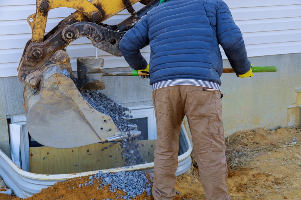 Bucket moving gravel in the window well on basement construction from window building materials.
