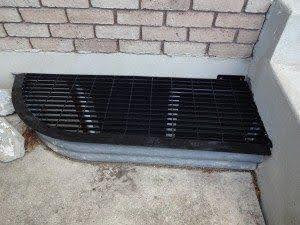 A metal grate embedded in a brick wall on the side of a building providing ventilation or access to utilities