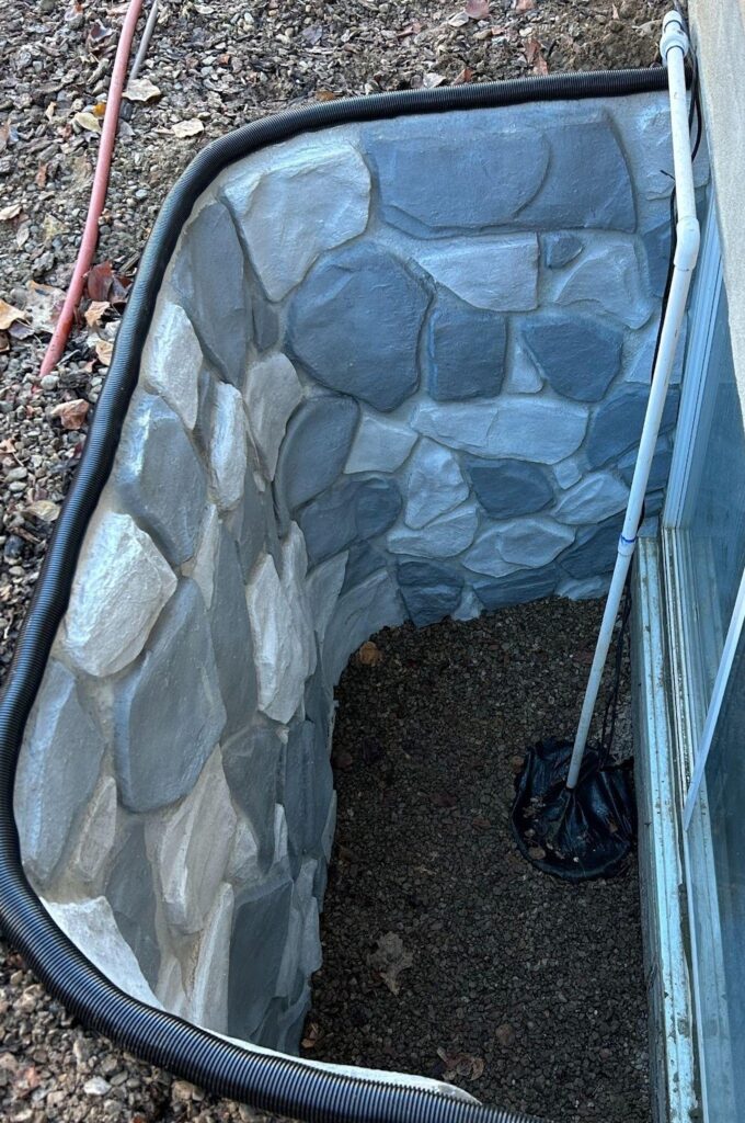 A stone wall featuring a pipe and a hose attached illustrating a functional outdoor water system