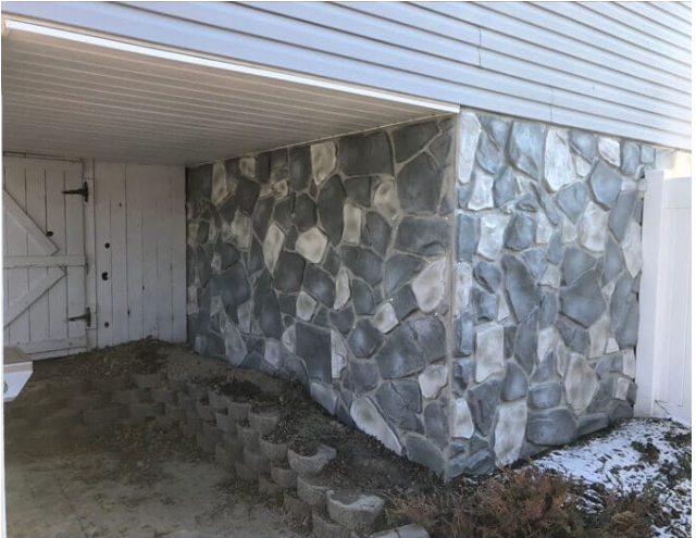 stone wall is being coated with gray paint showcasing a fresh update to its rustic texture