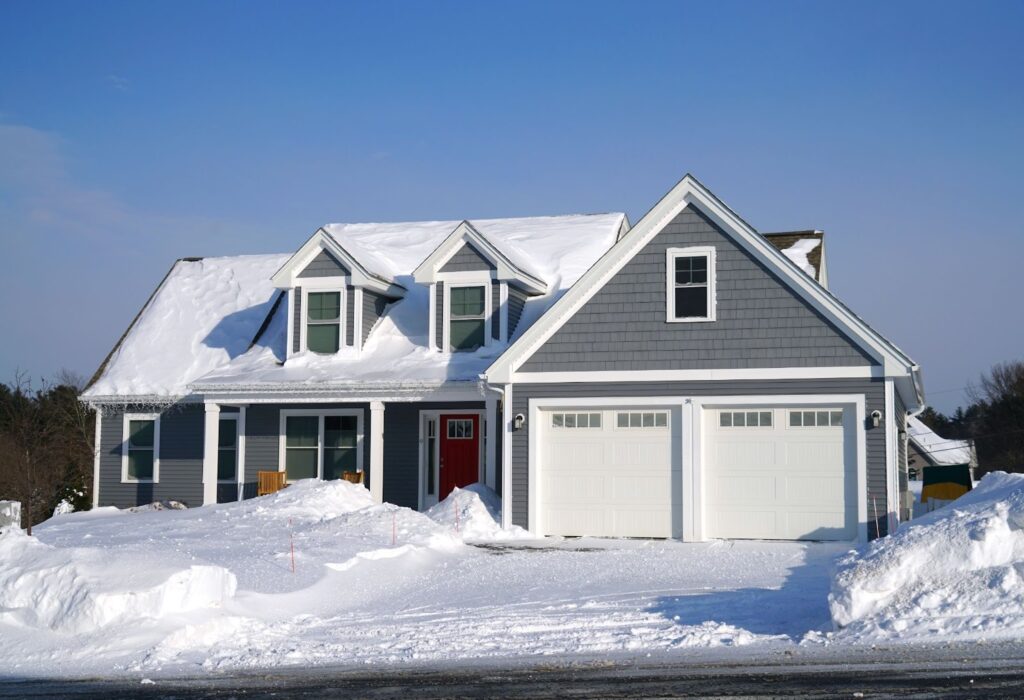 A large gray house with a snowy driveway, showcasing a winter scene with snow piled high.