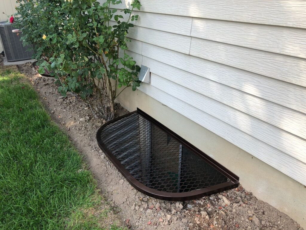 A black metal grate covering a basement window well on the side of a house.