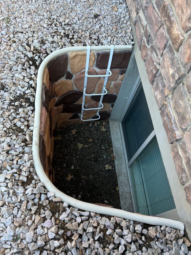 Egress window well featuring a stone-patterned liner, a white emergency escape ladder, and a gravel base.