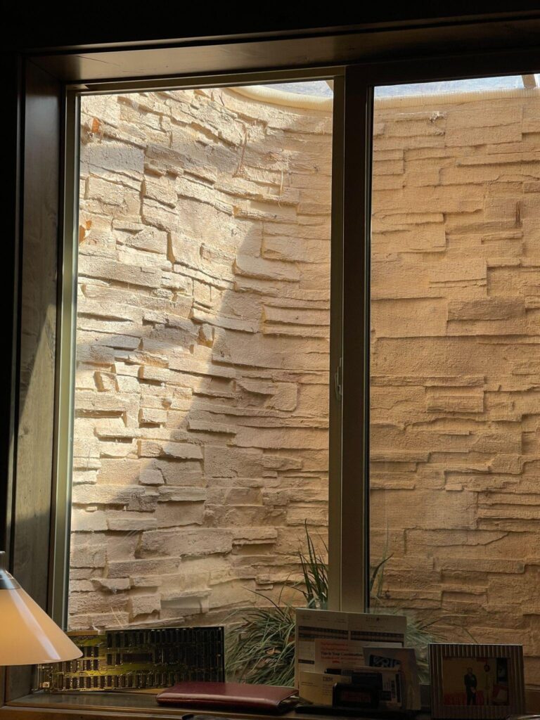 A window overlooking a wall and a desk highlighting a minimalistic office setting